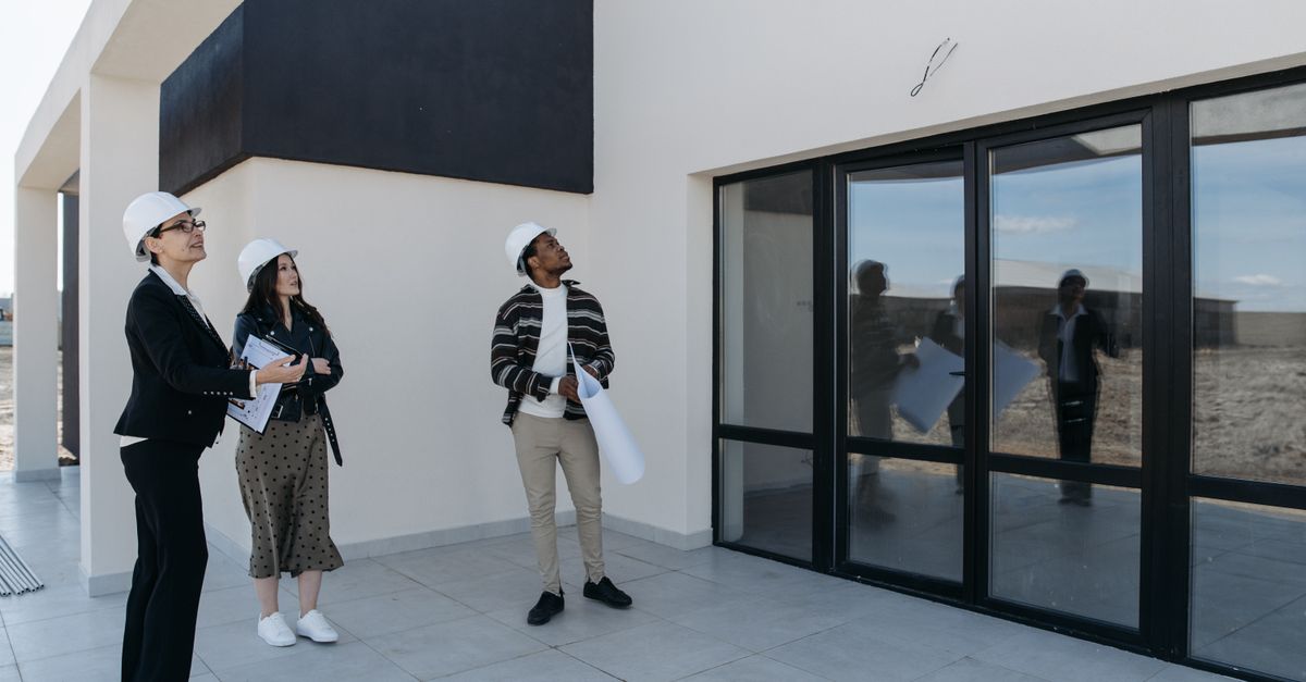 Architects in hard hats discuss the structure of a new building with large glass doors, suggesting a modern architectural design.